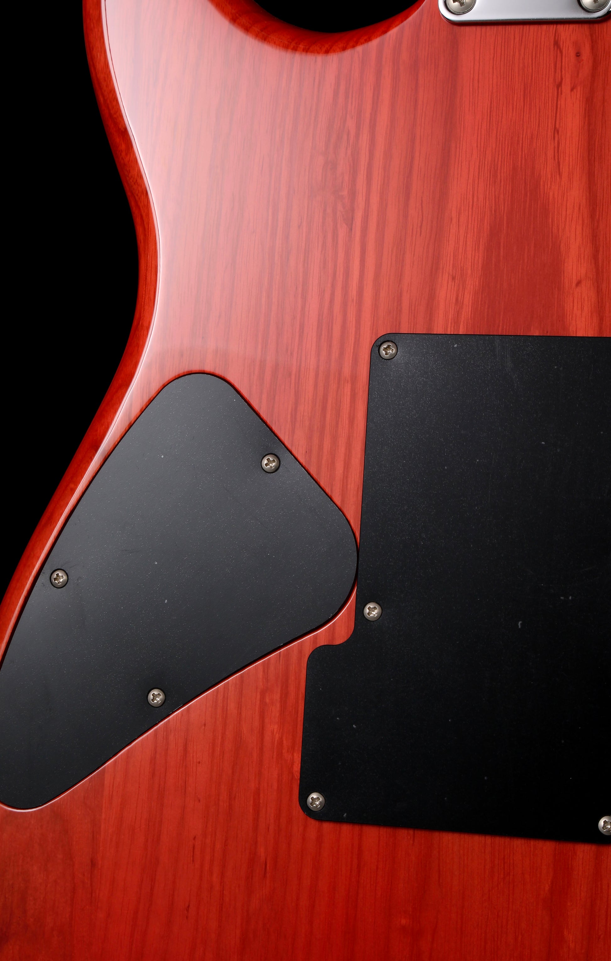 Fender Japan Michiya Haruhata Stratocaster Transparent Pink 2021: Close-up of an electric guitar body featuring a glossy red cherry wood finish, black pickguard, and a black plate with silver screws.
