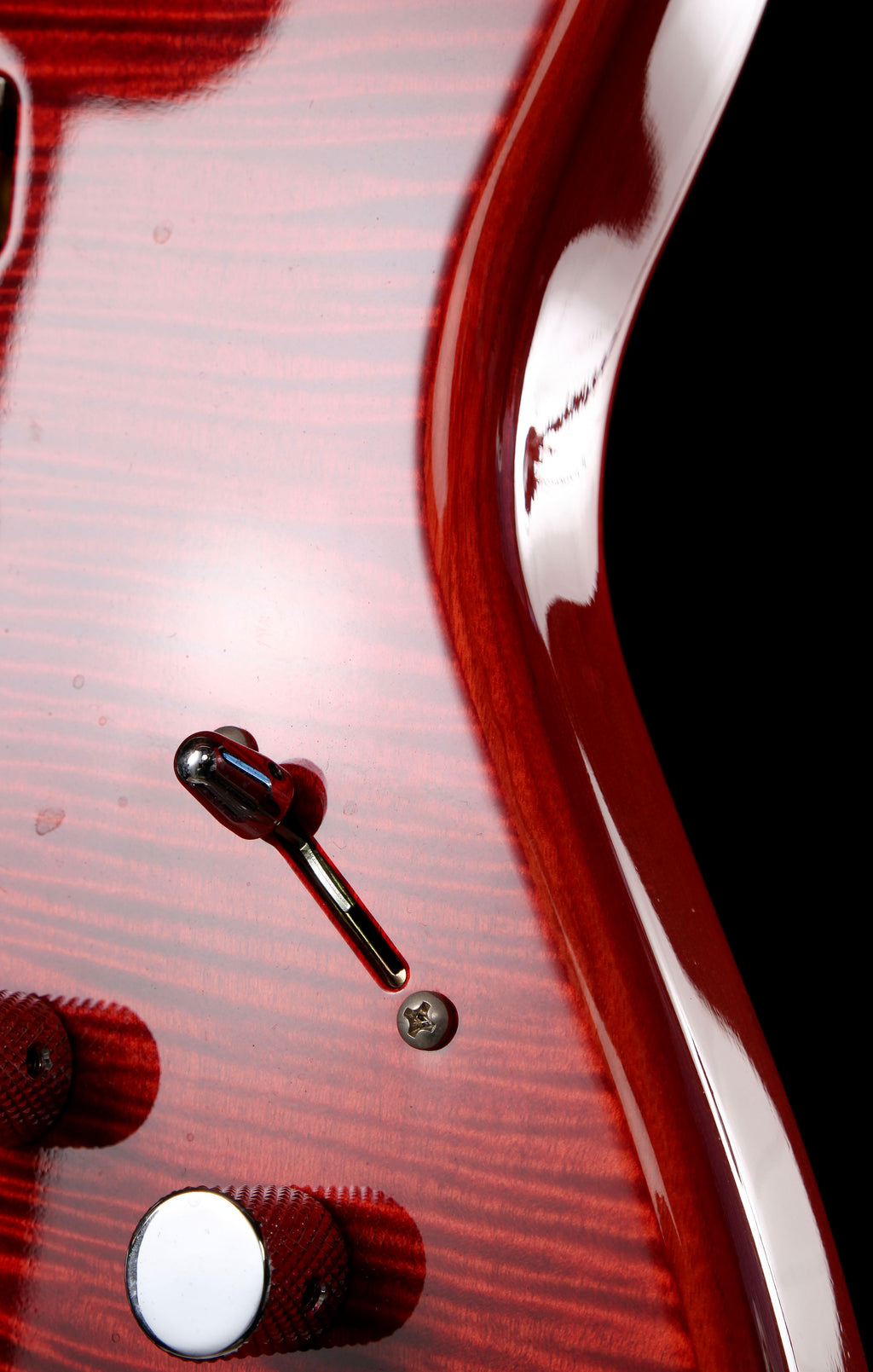 Fender Japan Michiya Haruhata Stratocaster Transparent Pink 2021: Close-up of a glossy red electric guitar body with a wood grain finish, showing part of the control knob, a screw detail, and the edge of the black pickguard area.
