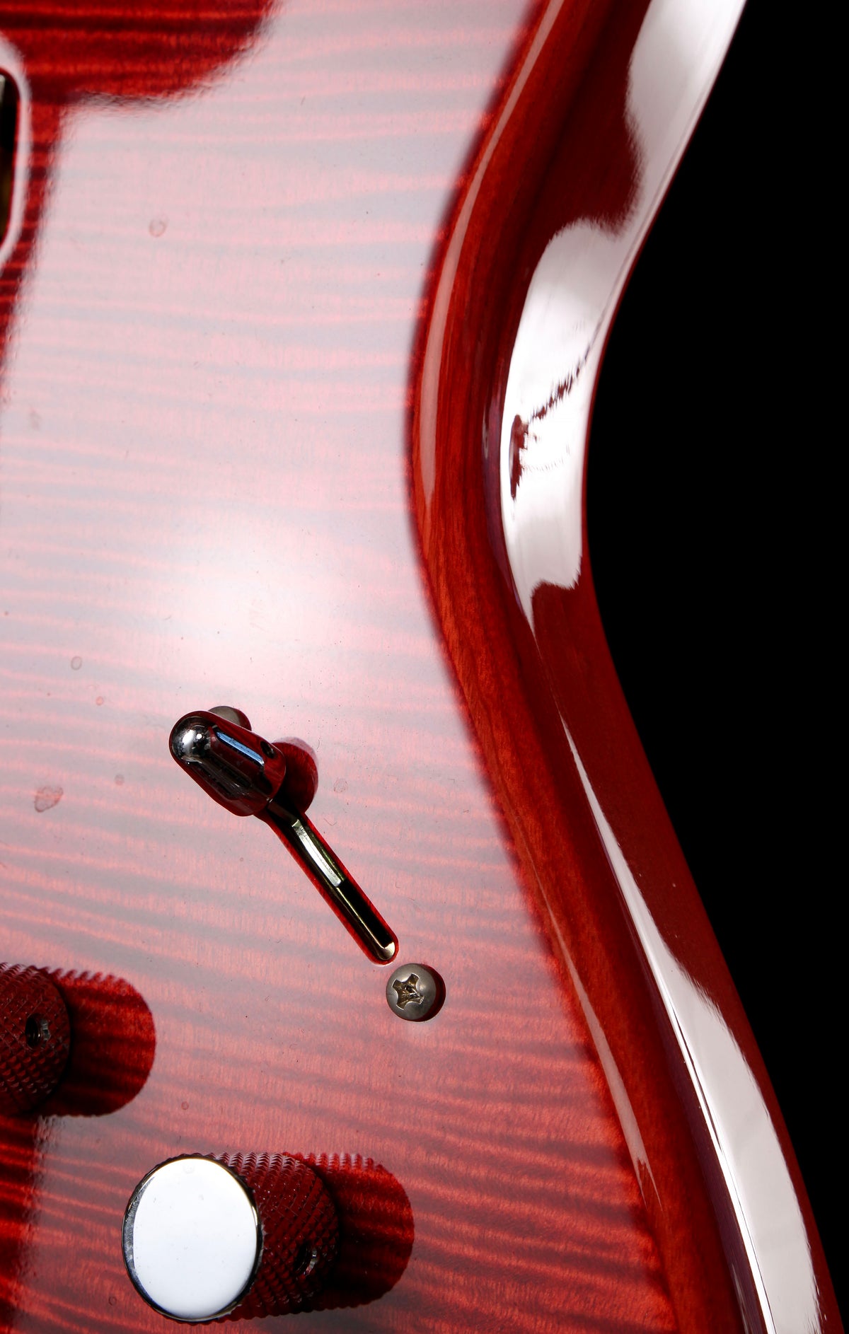 Fender Japan Michiya Haruhata Stratocaster Transparent Pink 2021: Close-up of a glossy red electric guitar body with a wood grain finish, showing part of the control knob, a screw detail, and the edge of the black pickguard area.