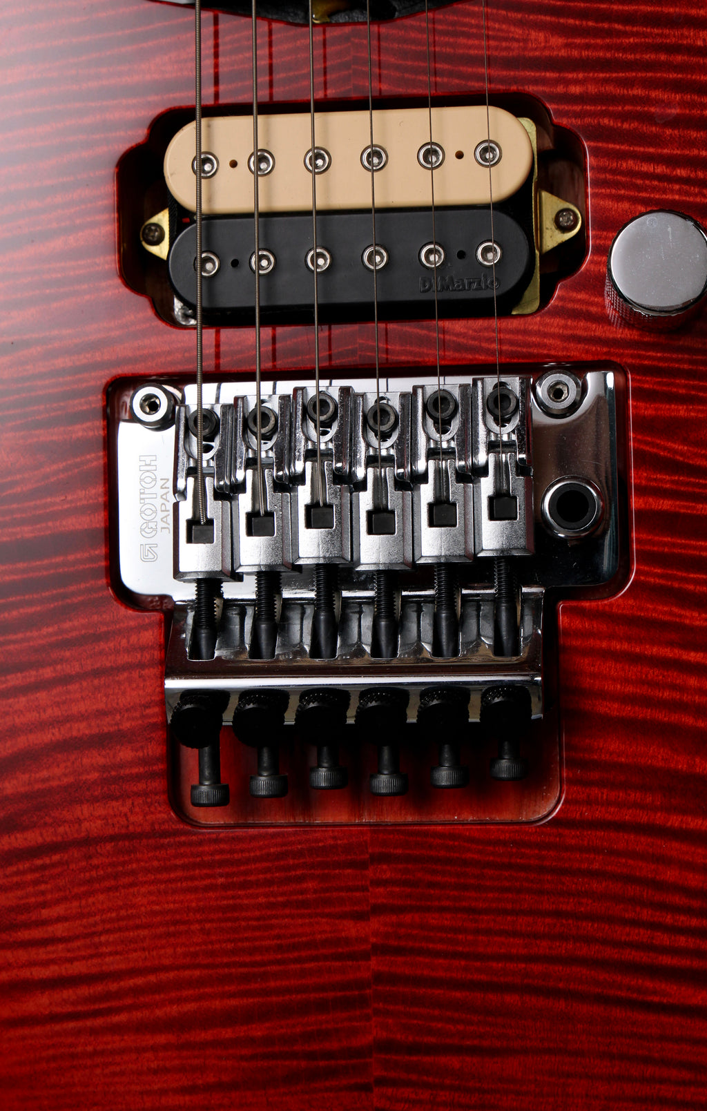 Fender Japan Michiya Haruhata Stratocaster Transparent Pink 2021: Close-up of a red electric guitar body showing a black and beige humbucker pickup, chrome bridge hardware, and part of a silver control knob against a red wood grain finish.