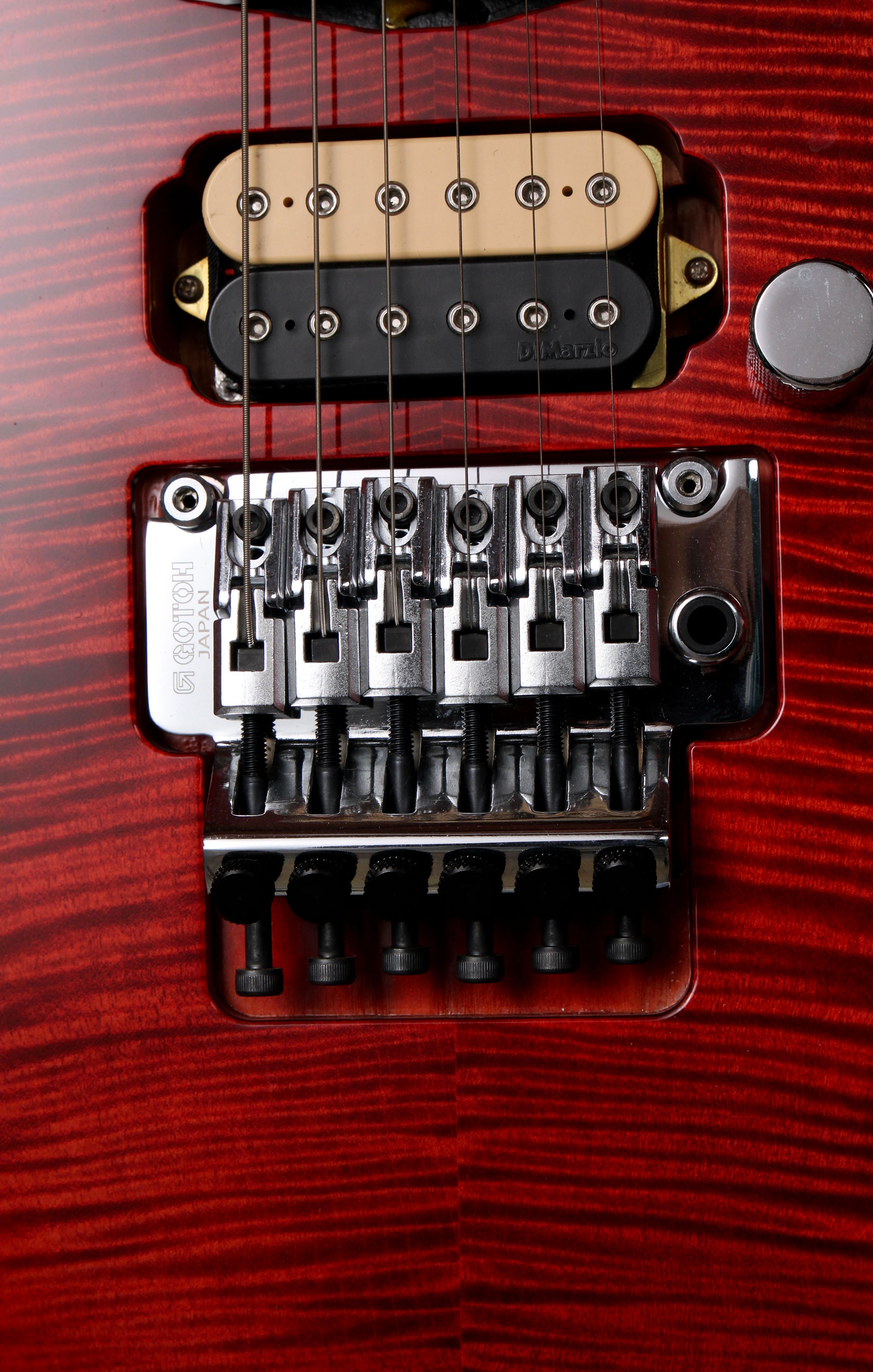 Fender Japan Michiya Haruhata Stratocaster Transparent Pink 2021: Close-up of a red electric guitar body showing a black and beige humbucker pickup, chrome bridge hardware, and part of a silver control knob against a red wood grain finish.
