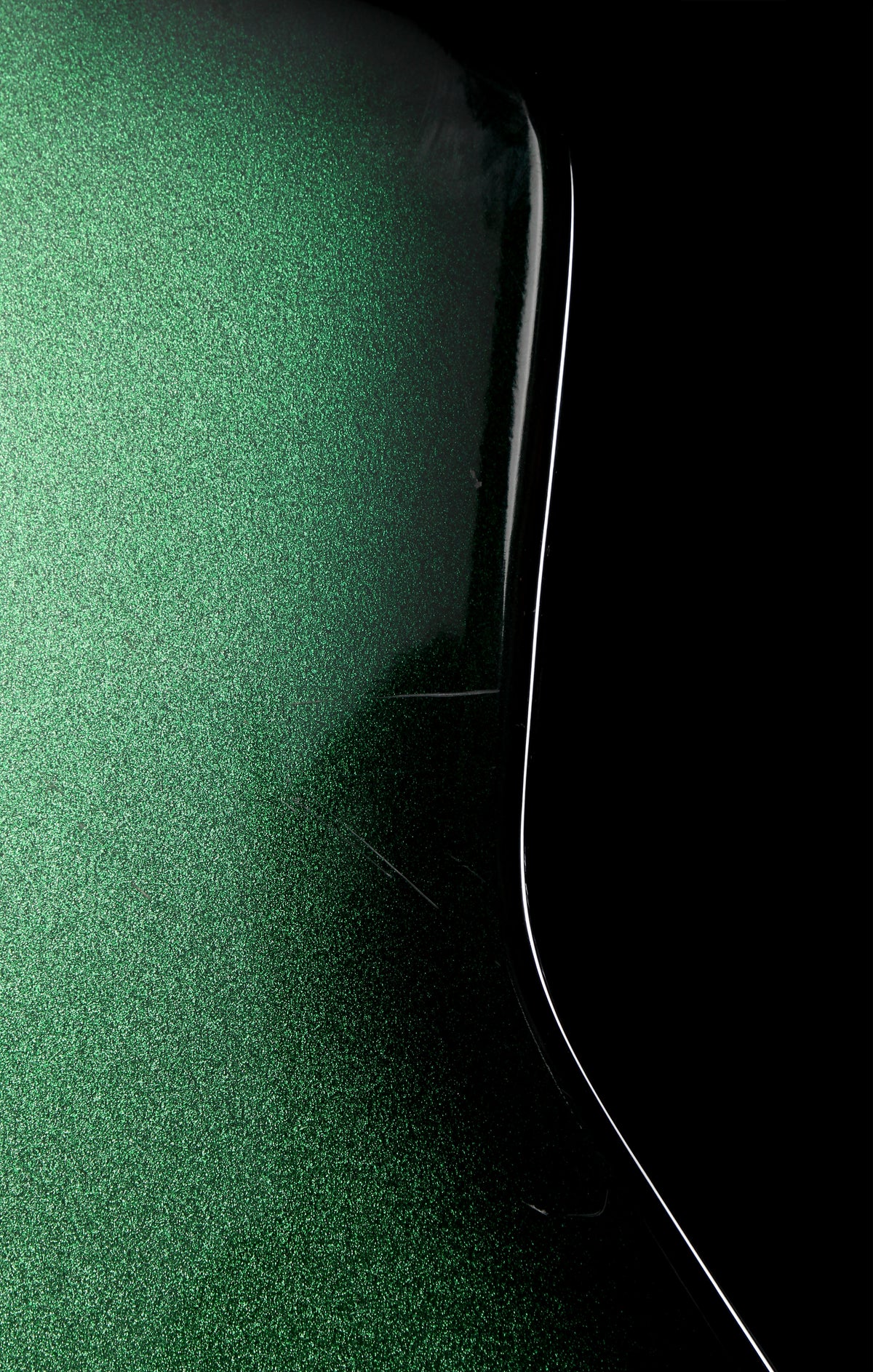 Fernandes EX Explorer Special Order SGS Sparkle Green Sunburst MIJ 1984: Close-up of a glossy dark green textured surface with a black curved edge and a thin white line against a black background.