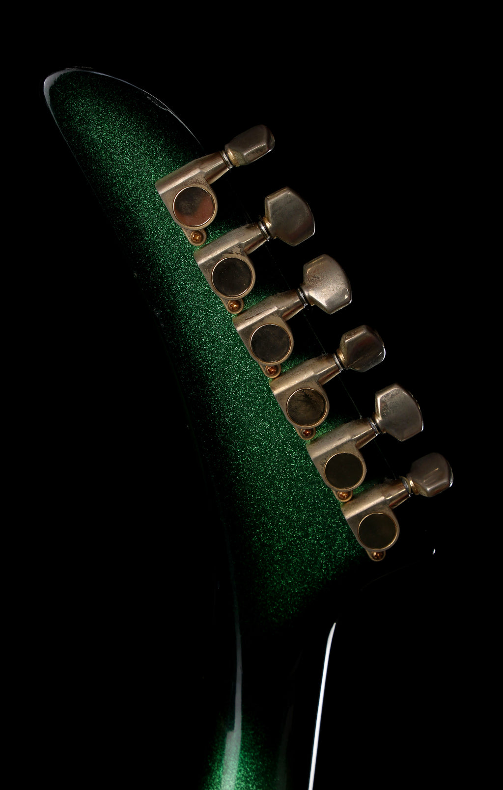 Fernandes EX Explorer Special Order SGS Sparkle Green Sunburst MIJ 1984: Close-up of a guitar headstock with a textured metallic green finish and six gold-toned tuning pegs against a solid black background.