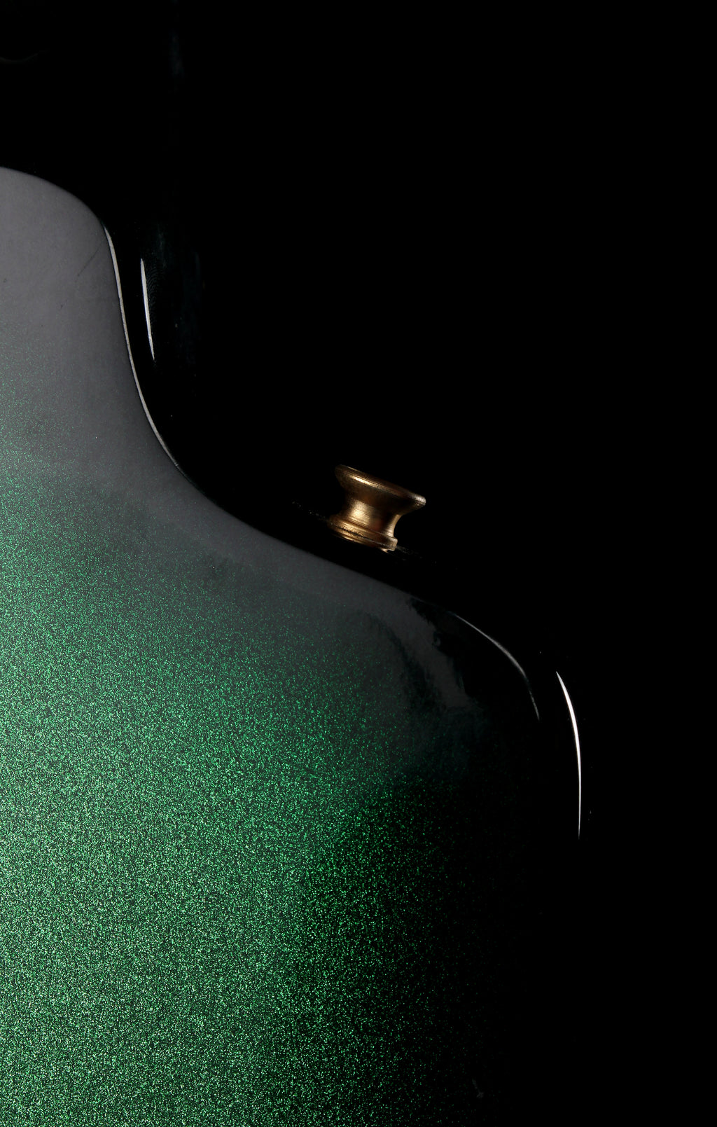 Fernandes EX Explorer Special Order SGS Sparkle Green Sunburst MIJ 1984: Close-up of a glossy green metallic product surface with a small gold-toned knob or connector against a black background.