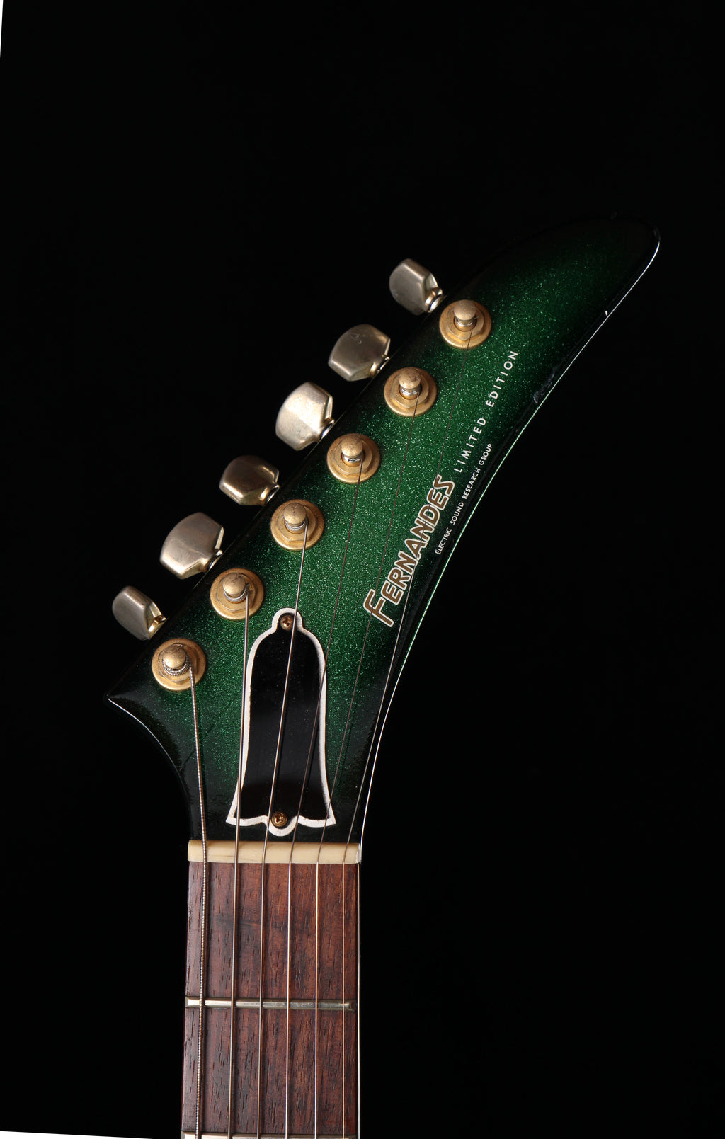Fernandes EX Explorer Special Order SGS Sparkle Green Sunburst MIJ 1984: Close-up of the headstock and upper neck of a green acoustic guitar against a black background. The headstock features gold tuning pegs, a white pickguard, and the 'Fernando' brand name printed in gold on the right side.