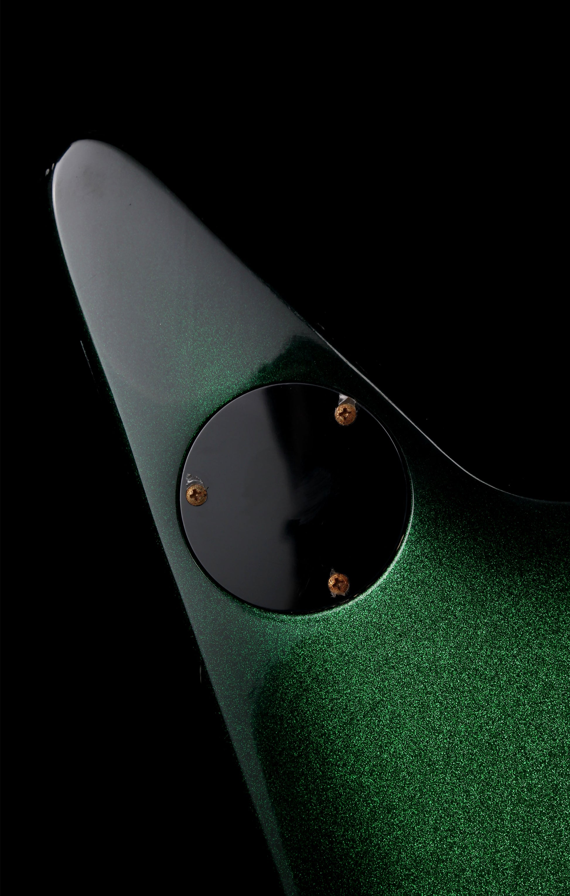 Fernandes EX Explorer Special Order SGS Sparkle Green Sunburst MIJ 1984: Close-up of a green glitter-finish guitar body with a black circular plate and small gold-toned screws, photographed against a black background.