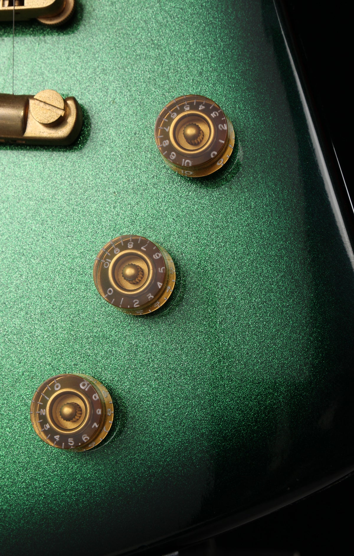 Fernandes EX Explorer Special Order SGS Sparkle Green Sunburst MIJ 1984: Close-up of a green electric guitar body showing three round gold-toned control knobs on a textured metallic green surface.