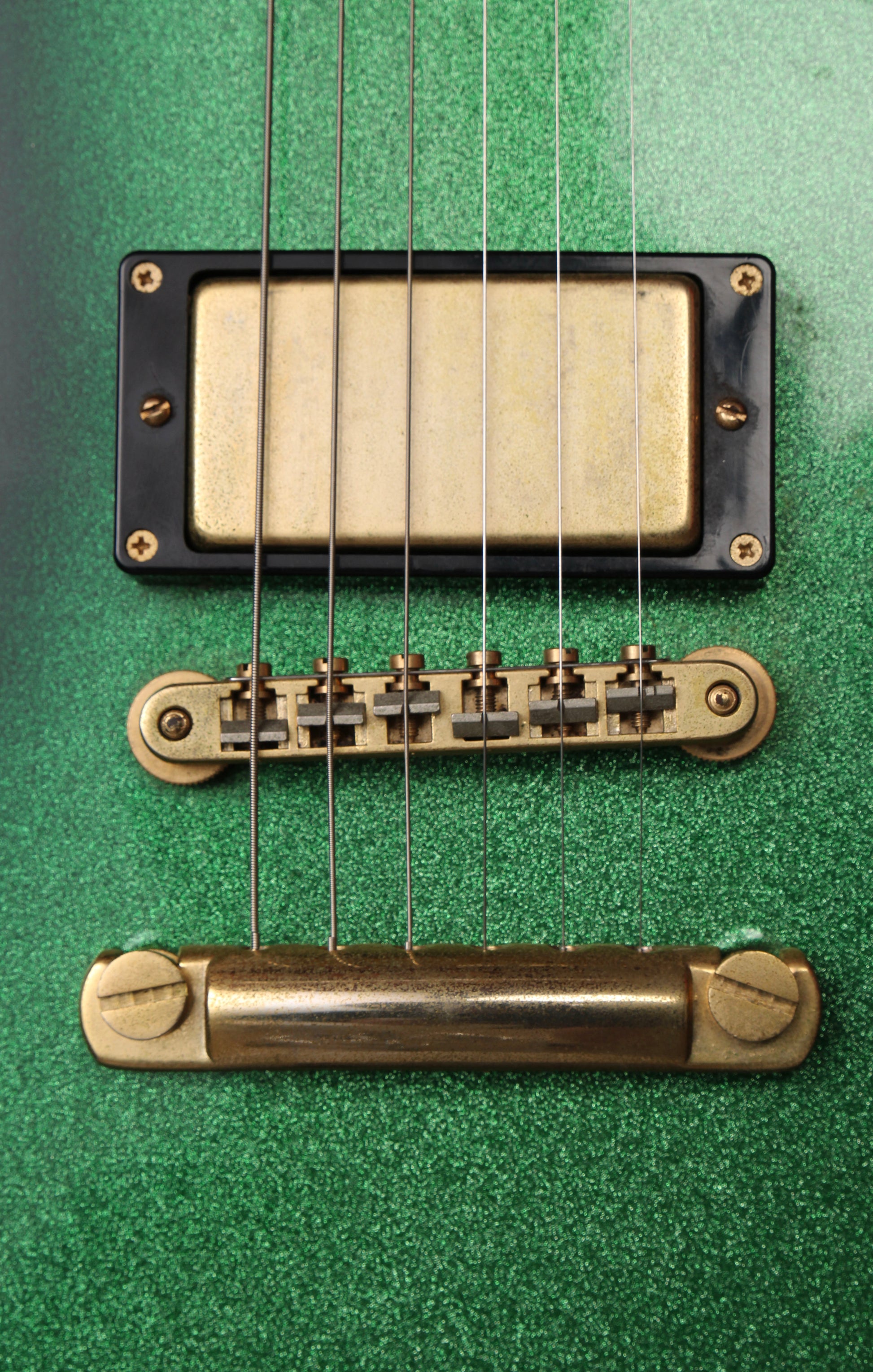 Fernandes EX Explorer Special Order SGS Sparkle Green Sunburst MIJ 1984: Close-up of a six-string electric guitar body showing a black and gold humbucker pickup, a gold bridge, and a gold tailpiece against a textured green finish.