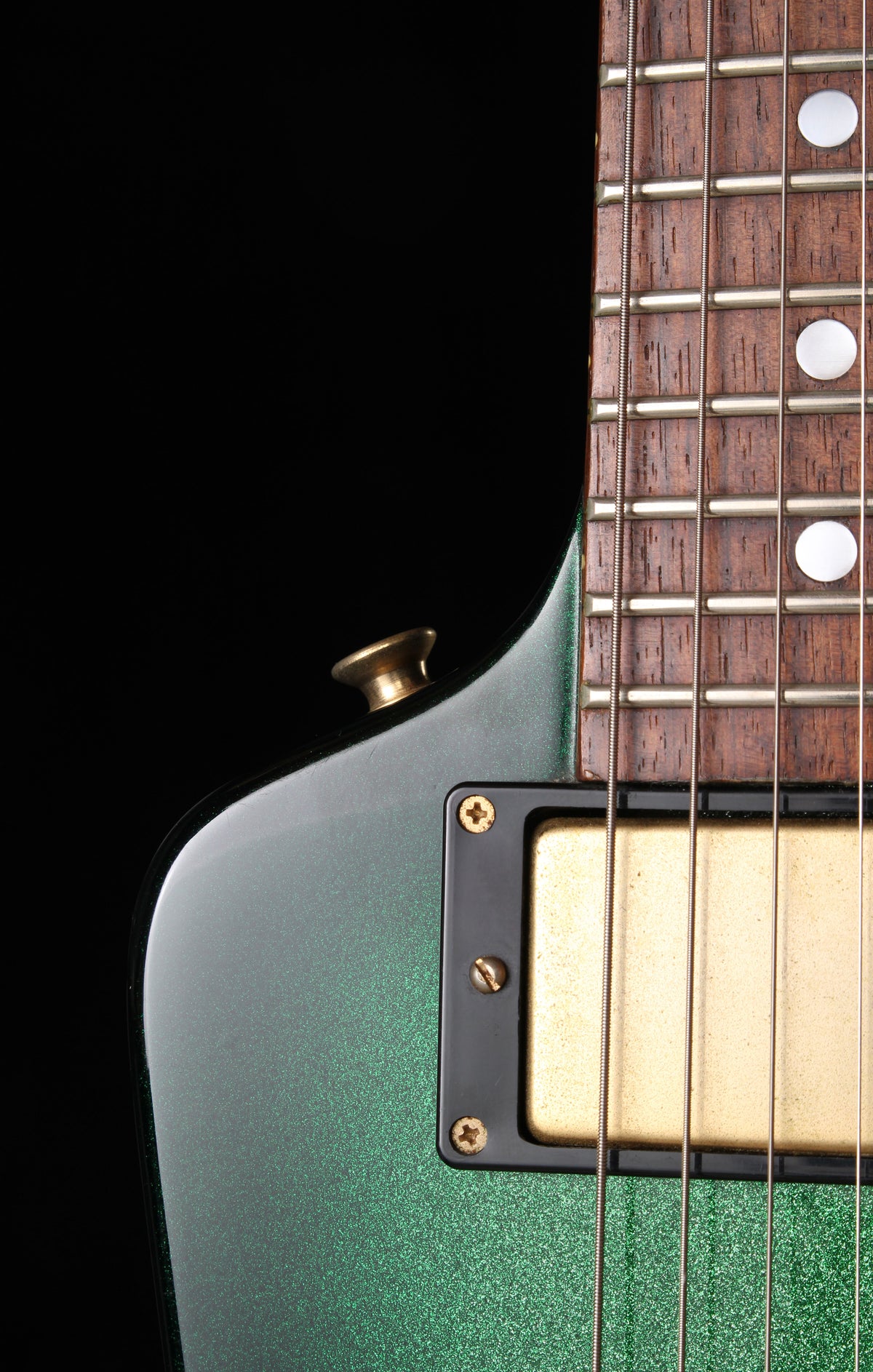 Fernandes EX Explorer Special Order SGS Sparkle Green Sunburst MIJ 1984: Close-up of an electric guitar body and neck, showing a metallic green glitter finish, a gold humbucker pickup, and a dark wood fretboard against a black background.